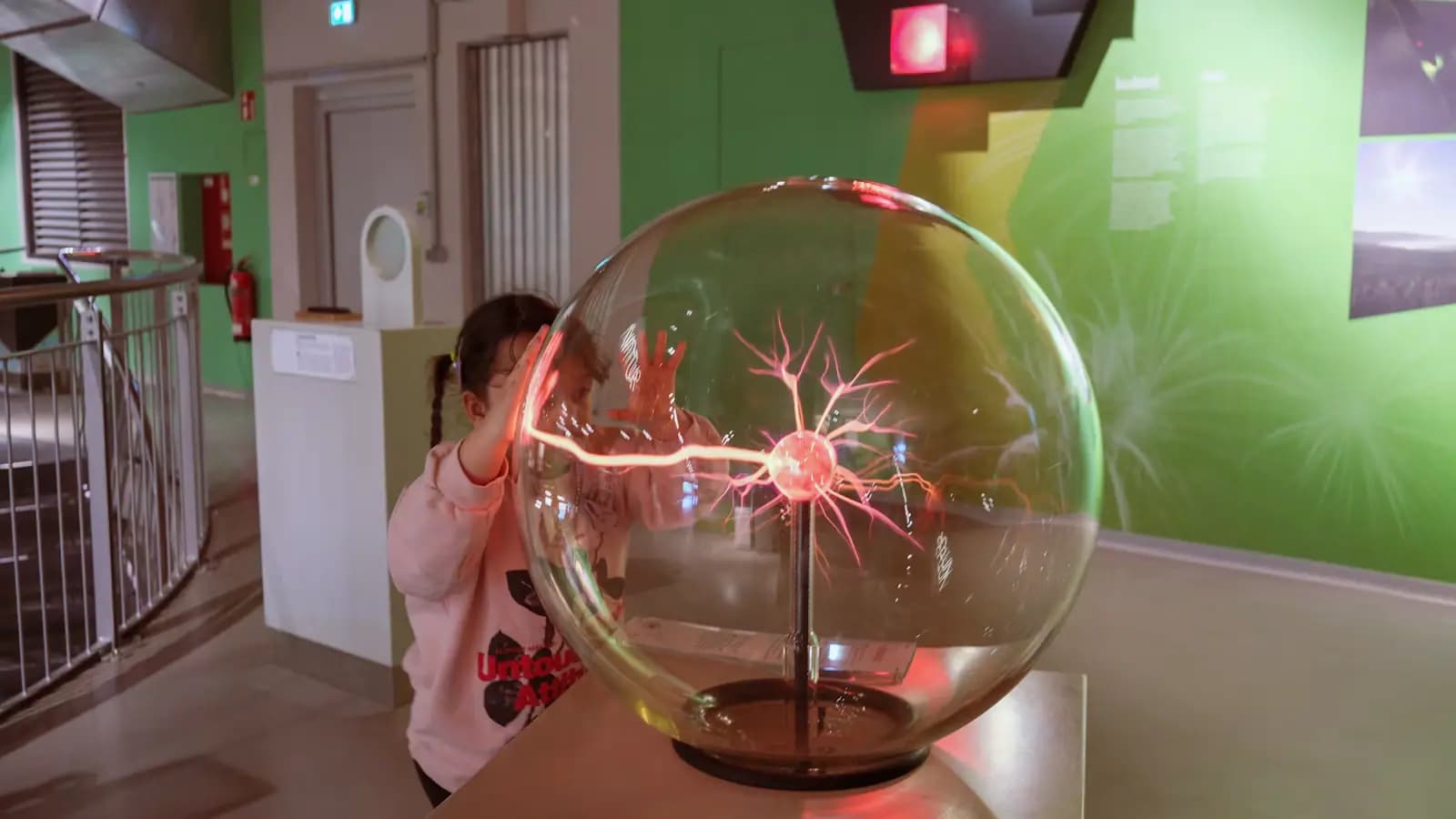 A young child with both hands on a glowing plasma ball in a hands-on science exhibit