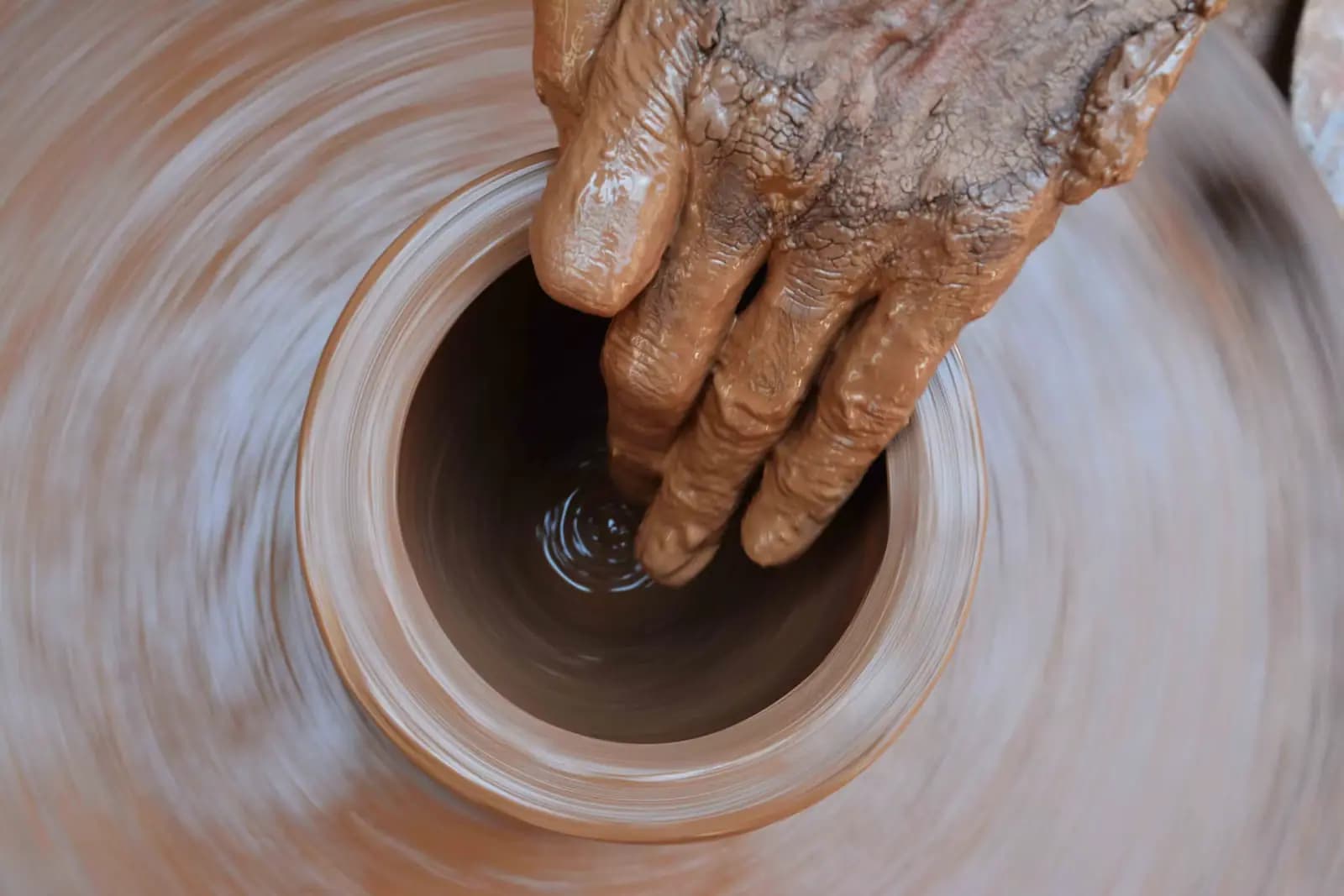A potter's hands shaping wet clay on a spinning wheel